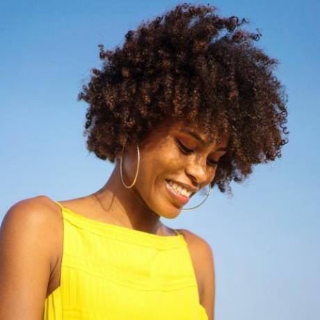 muotokuva nuoresta mustasta naisesta, jolla on yllään keltainen mekko, hymyilevä